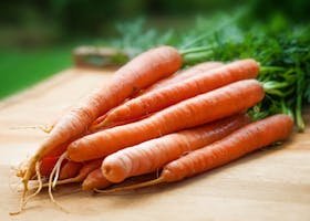 A bunch of fresh organic carrots on a wooden surface, perfect for healthy cooking.