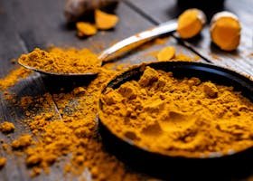 Close-up of vibrant turmeric powder with root on rustic wooden table, emphasizing texture and color.