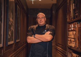 Bald chef standing confidently indoors, arms crossed, in a stylish hallway.